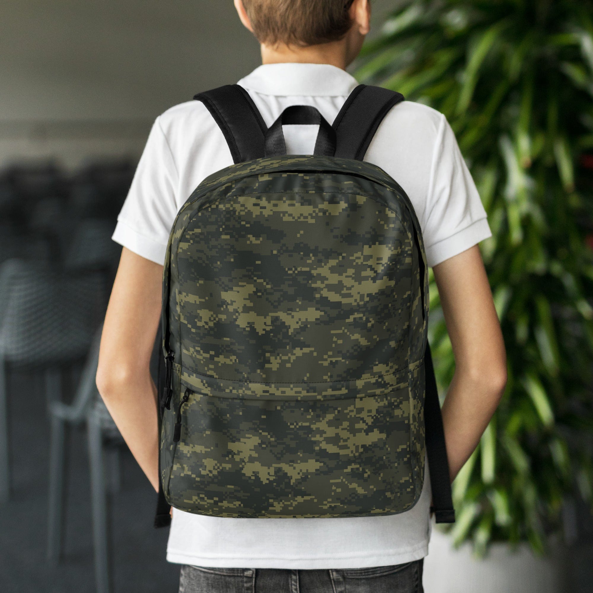 Digital camouflage backpack worn on back, with top handle and front zipper pocket.