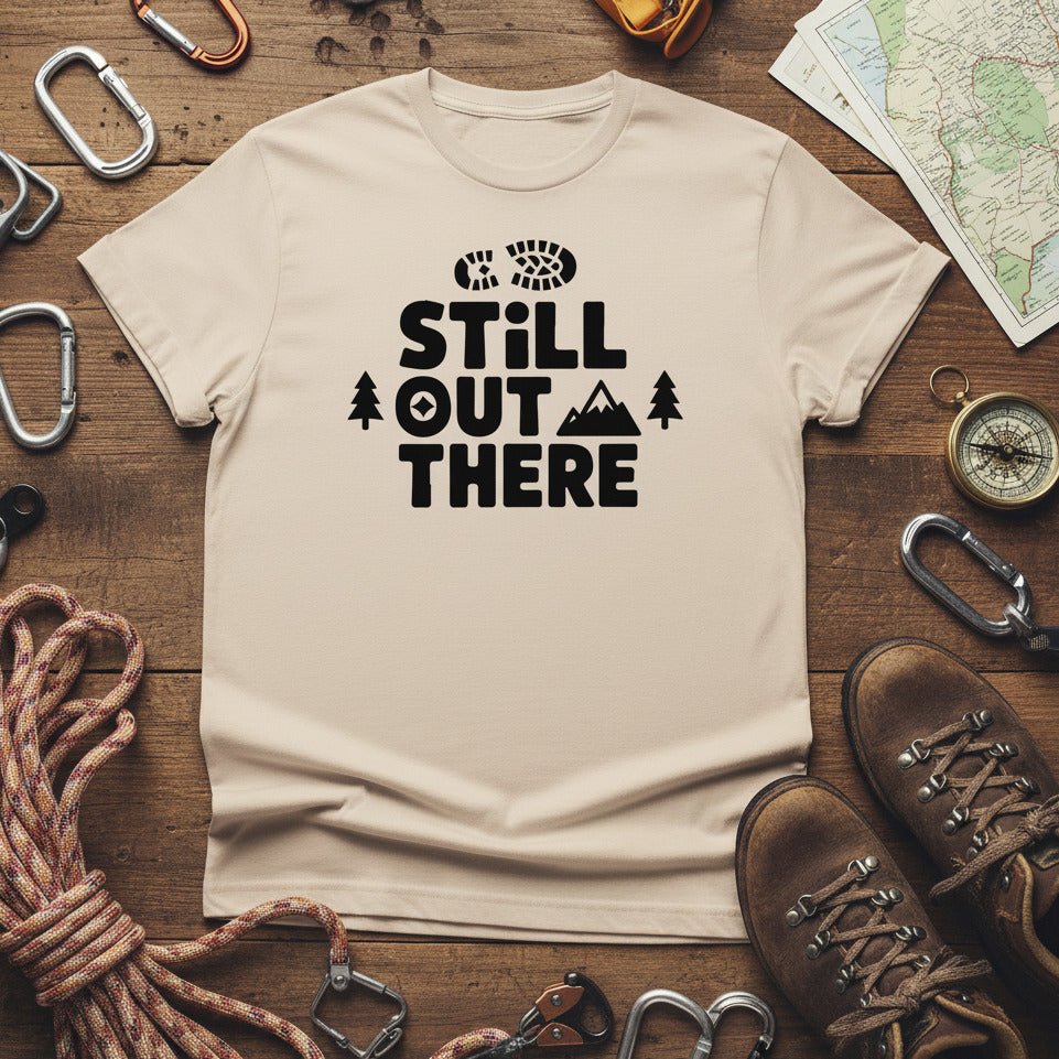 Cream hiking T-shirt with black “Still Out There” logo graphic and paw-tree icon