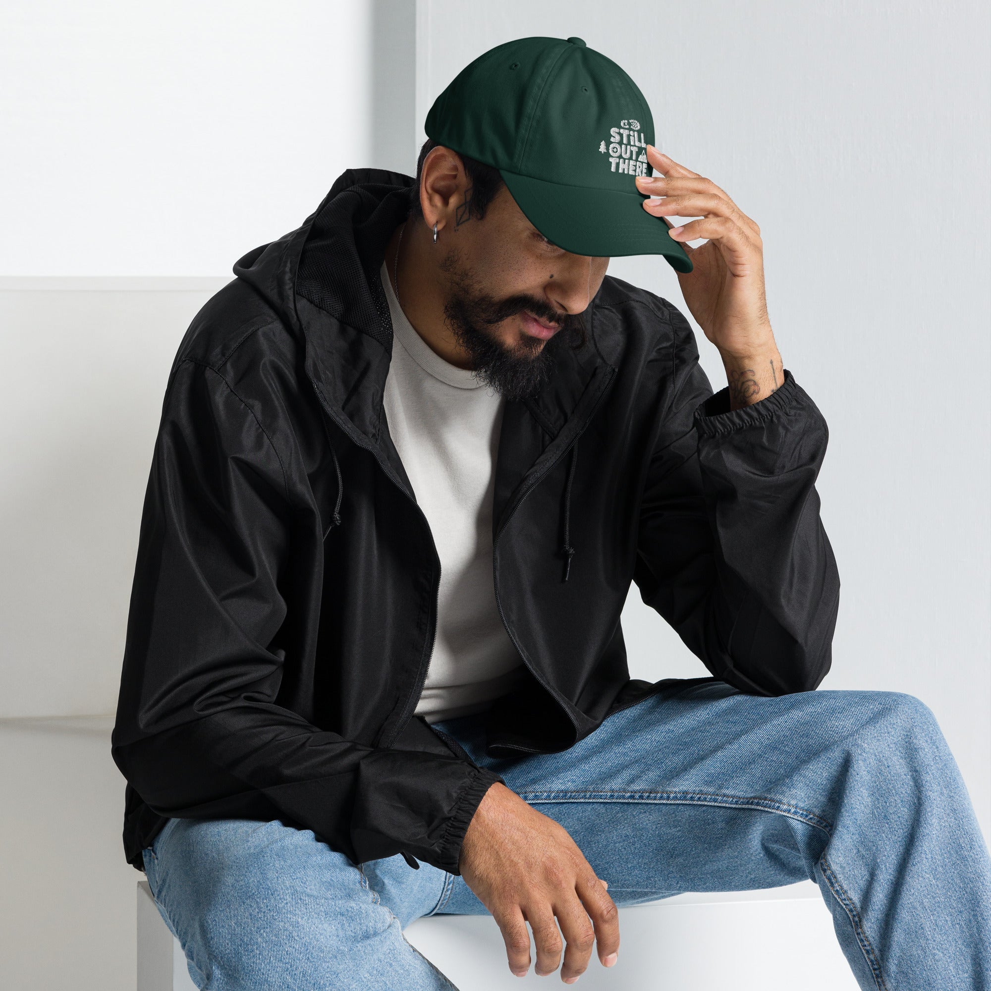 Green dad hat with embroidered “STILL OUT THERE” logo on front and curved brim.