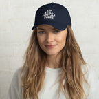 Navy dad hat with embroidered “STILL OUT THERE” logo on front and curved brim.