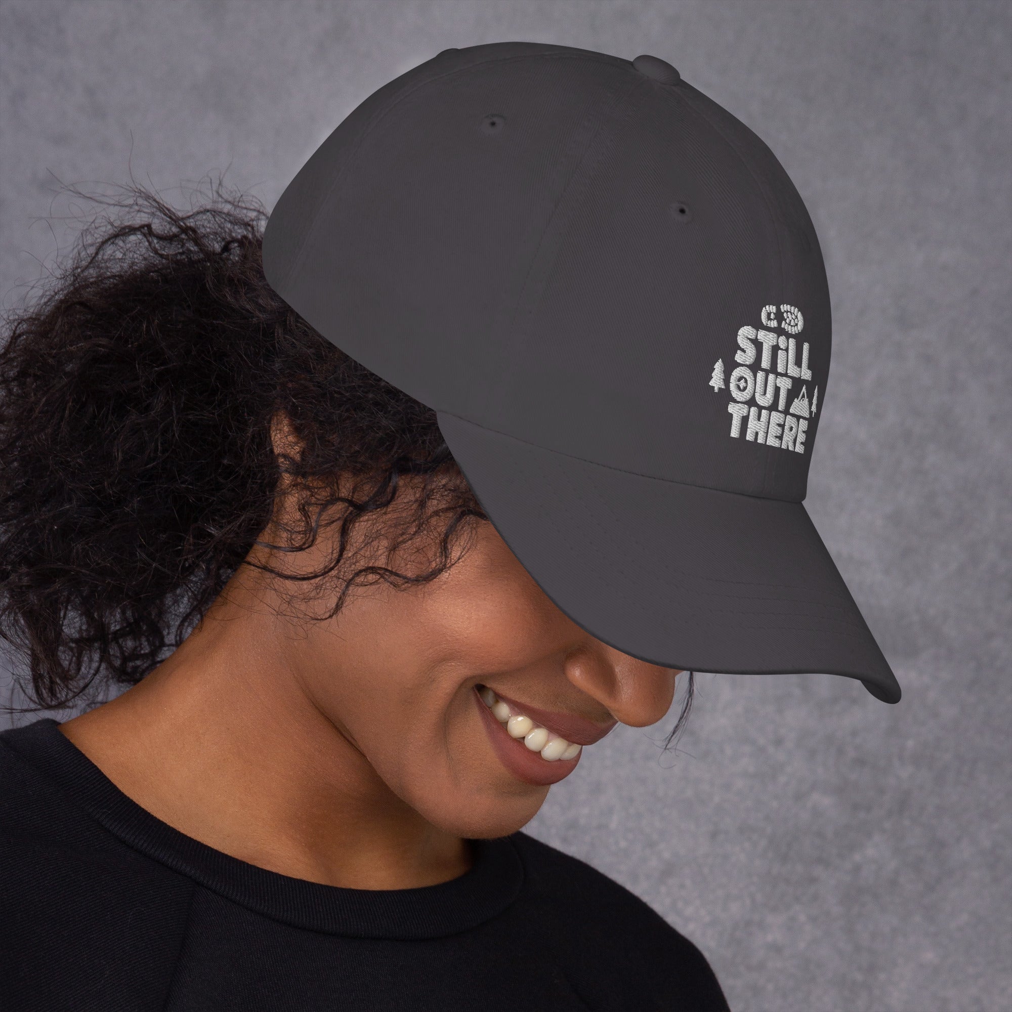 Gray baseball cap with embroidered “STILL OUT THERE” logo on front and curved brim.