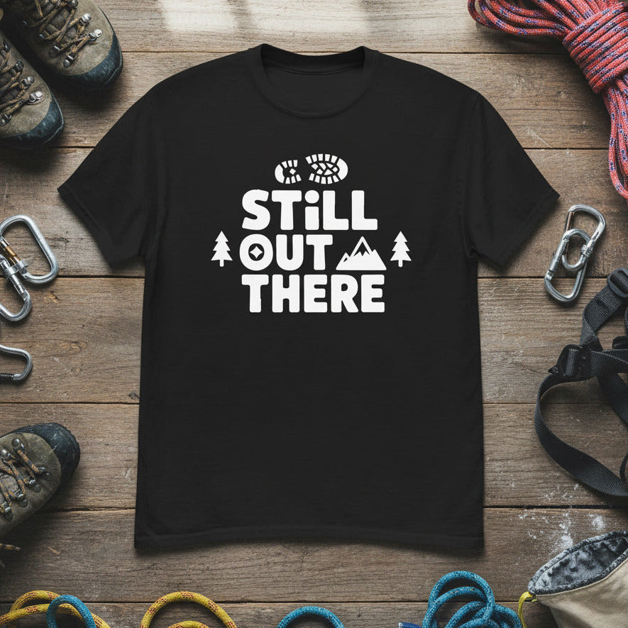 Black hiking T-shirt with white “STILL OUT THERE” logo and trees graphic