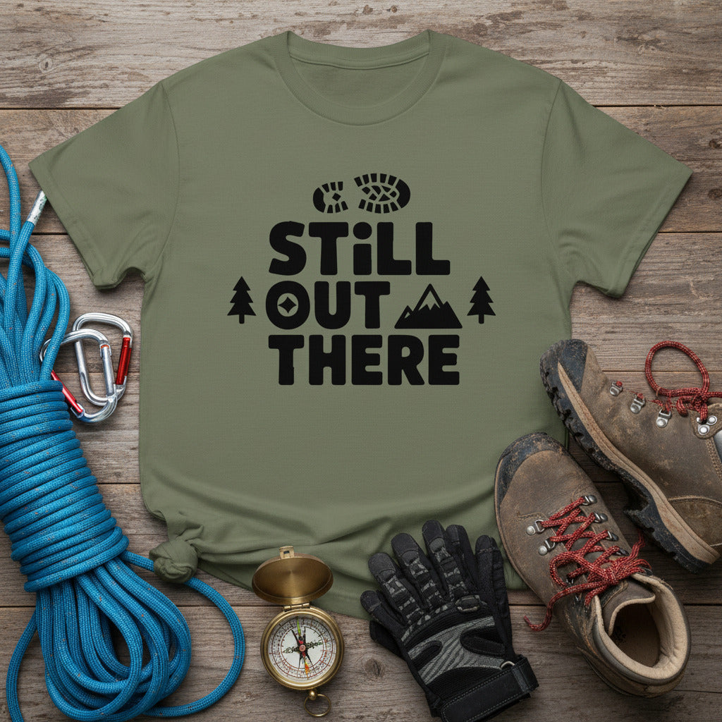 Olive green hiking T-shirt with black “STILL OUT THERE” logo and pine trees