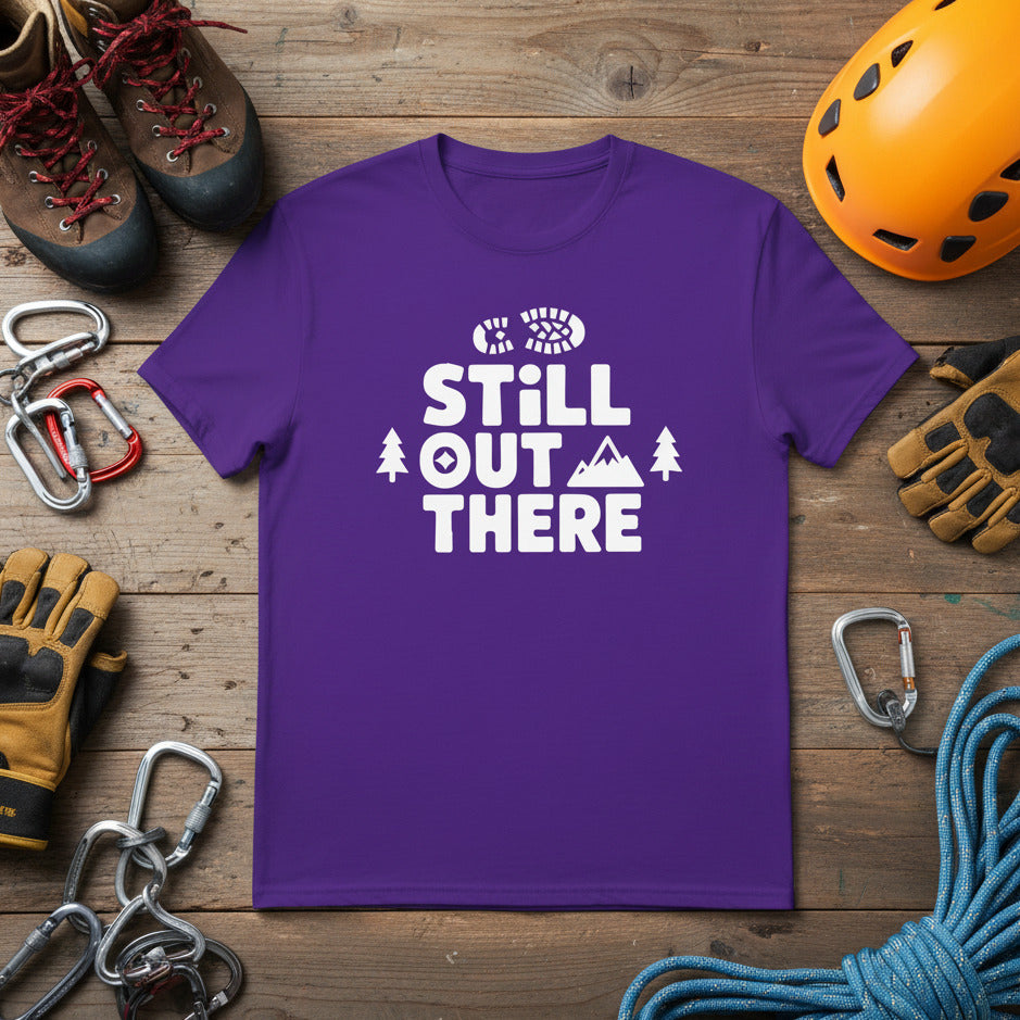 Purple hiking T-shirt with white “STILL OUT THERE” logo and tree and mountain icons
